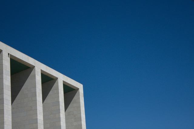 Concrete building facade with a repeating pattern of triangular openings against a clear sky.