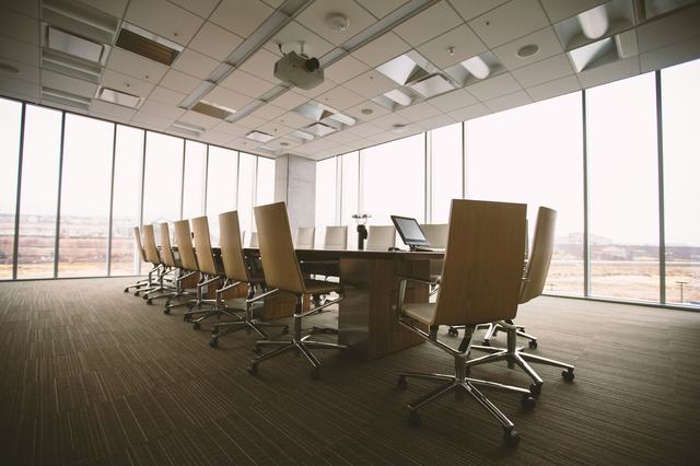 An empty boardroom with a long table and chairs beside floor-to-ceiling windows.